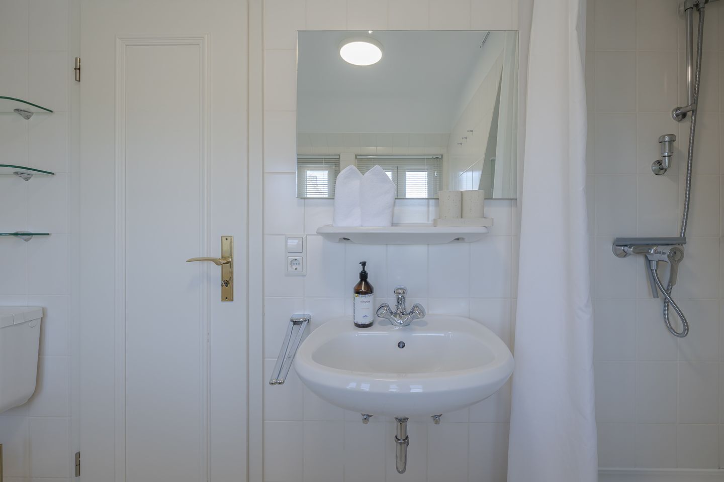 A bathroom with a white sink, a mirror, a shower, and a door with a brass handle.