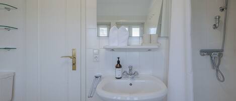 A bathroom with a white sink, a mirror, a shower, and a door with a brass handle.