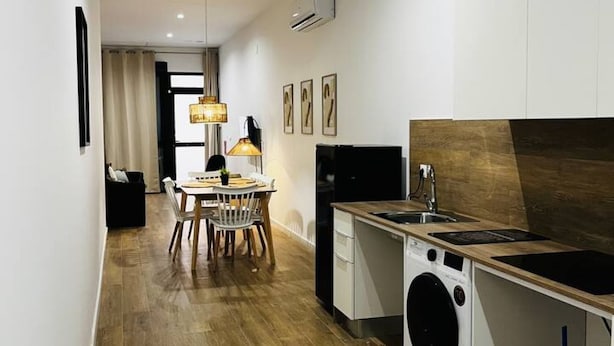 Cocina compacta con lavadora, comedor con mesa y sillas, y una lámpara colgante.