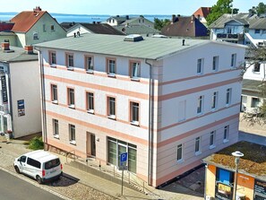 A multi-story building with a flat roof, several windows, and a parking area with a white van.