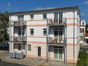 Un immeuble résidentiel à plusieurs étages, doté de balcons, d’un abri pour voitures et d’un petit jardin.