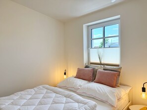 A bedroom with a bed, pillows, a window, and two wall-mounted lamps. - Harbor master Björn - Spacious living above the rooftops of Sassnitz (Sassnitz)