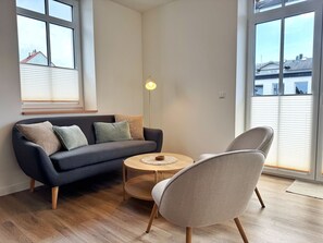Un salon moderne avec un canapé gris foncé, une table basse ronde en bois et un fauteuil gris clair.