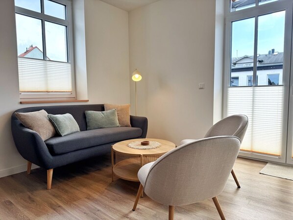 A modern living room with a dark grey sofa, a round wooden coffee table, and a light grey armchair. - Harbor master Björn - Spacious living above the rooftops of Sassnitz (Sassnitz)