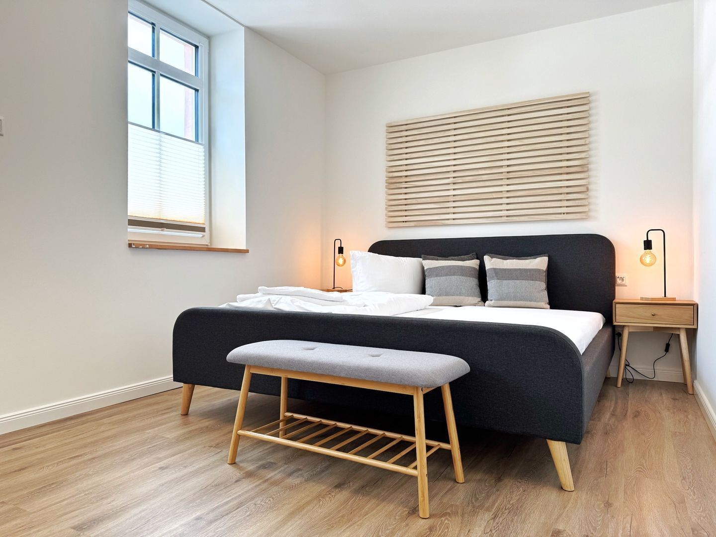 A modern bedroom with a bed, bedside tables, a bench, and a window.