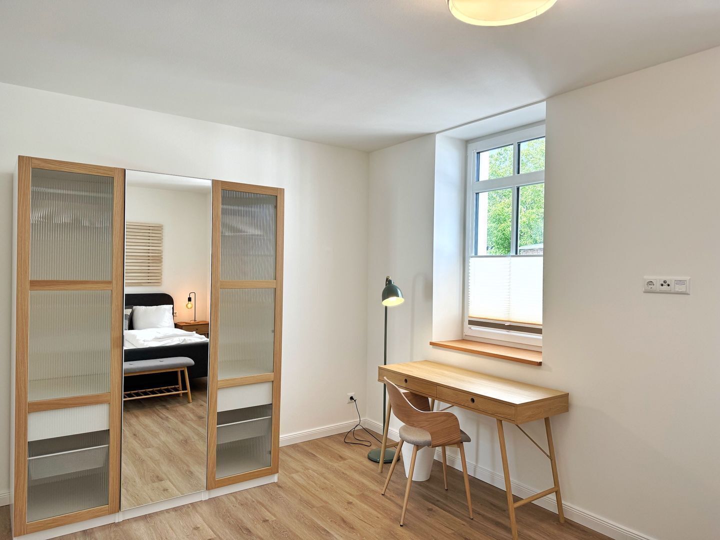 A bedroom with a bed, a desk, and a window.
