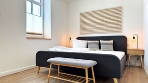 A modern bedroom with a bed, bedside tables, a bench, and a window. - Harbor master Lasse - Spacious, cozy & maritime above the rooftops of (Sassnitz)