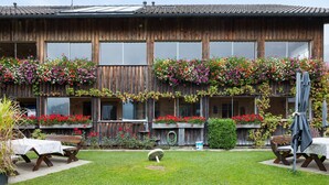 A wooden building with large windows, a balcony with flowers, and outdoor seating. - Room 'Zirbengeist' with Mountain View, Shared Garden and Wi-Fi (Sibratsgfäll)