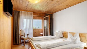A wooden-paneled room with two beds, a chair, and a window with curtains. - Room 'Zirbengeist' with Mountain View, Shared Garden and Wi-Fi (Sibratsgfäll)