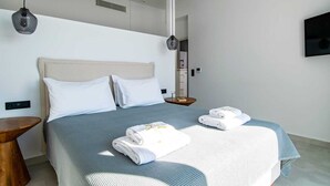 Moderni hotellihuone, jossa on suuri sänky, kaksi tyynyä, yöpöytä, puinen yökaappi, riippuvalaisin ja seinälle asennettu litteänäyttöinen televisio.