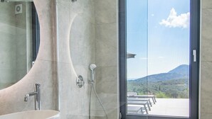 A modern bathroom with a large sink, glass shower enclosure, and a view of a mountainous landscape through a large window. - 5-Bedroom Luxury Villas in Lefkada (Lefkada)
