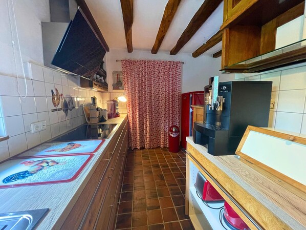 Une cuisine avec un mur recouvert de carreaux, des poutres apparentes en bois, un réfrigérateur rouge, une machine à café et un sol carrelé.