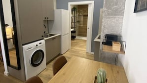 Una cocina compacta con lavadora, un comedor con mesa y sillas, y un pequeño estante.