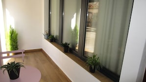 Un balcón con suelo de madera, una silla rosa y varias macetas con plantas.