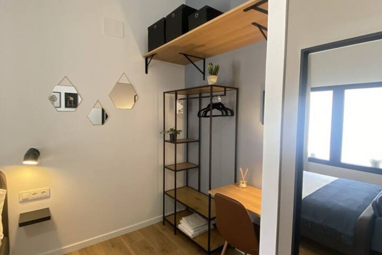 Ein kleines Zimmer mit Schreibtisch, Regalen und einem Bett.
