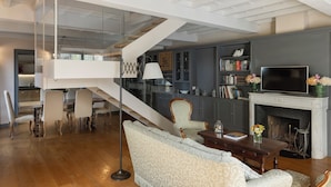 A modern living room with a staircase, a fireplace, and a dining area with chairs and a table.