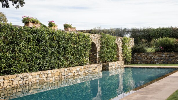 A swimming pool with stone walls and a stone bridge.