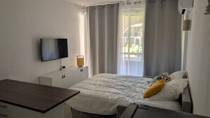 Quarto de hotel com cama, escrivaninha, televisão e janela com cortinas.