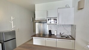 Uma cozinha moderna com armários brancos, uma geladeira de aço inoxidável, micro-ondas e pia.