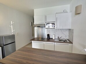 A modern kitchen with white cabinets, a stainless steel refrigerator, a microwave, and a sink.