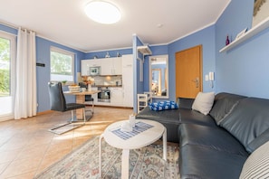 A living room with a black leather sofa, a white coffee table, a patterned rug, and a kitchen area with white cabinets and a microwave. - Cozy vacation apartment "Ostseegold" with terrace (Ückeritz)