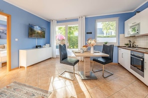 A modern kitchen with white cabinets, a dining table with chairs, a TV mounted on the wall, and a large window. - Cozy vacation apartment "Ostseegold" with terrace (Ückeritz)