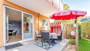 Une terrasse extérieure avec une table et des chaises, un parasol rouge et une porte-fenêtre coulissante donnant sur une pièce intérieure.