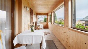 Interior de fusta amb taula preparat per dinar, una cadira i finestra que mostra edificis i vegetació.