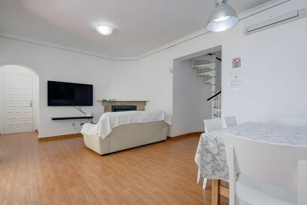 A modern living room with a flat-screen TV, a sofa, a dining table, and a staircase. - Villa 'Guadiaro' with Mountain View, Wi-Fi and Air Conditioning (Marbella)