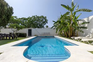 A rectangular swimming pool with blue tiles, surrounded by white walls, a grassy area, and white lounge chairs. - Villa 'Guadiaro' with Mountain View, Wi-Fi and Air Conditioning (Marbella)