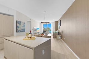 A modern kitchen with a central island, a dining area with a view, and a living space with a sofa and a TV.