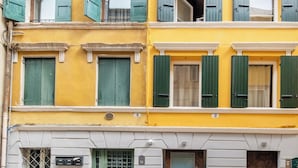 A multi-story building with yellow facades, green shutters, and a stone-paved ground. - ApartmentsArena - Mustacchi Rooms (Verona)