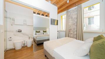 A modern bedroom with a wooden ceiling, a large bed with white bedding, a TV mounted above the bed, and a bathroom with a glass shower enclosure.