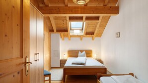 A bedroom with a wooden ceiling, a skylight, a bed, a nightstand, and a wardrobe.