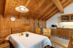 A wooden interior with a dining table set for two, a kitchen with wooden cabinets, and a clock on the wall.