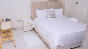 Une chambre bien rangée, avec un lit, une petite table de chevet, une chaise et un sol blanc.
