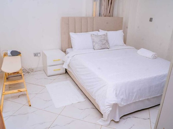 A neatly arranged bedroom with a bed, a small bedside table, a chair, and a white floor.