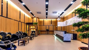 Zona de recepción con pared de paneles de madera, mostrador de recepción y asientos con sillas tapizadas en negro.