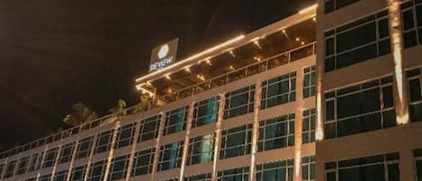 A multi-story hotel with a modern facade, illuminated signage, and a covered parking area.