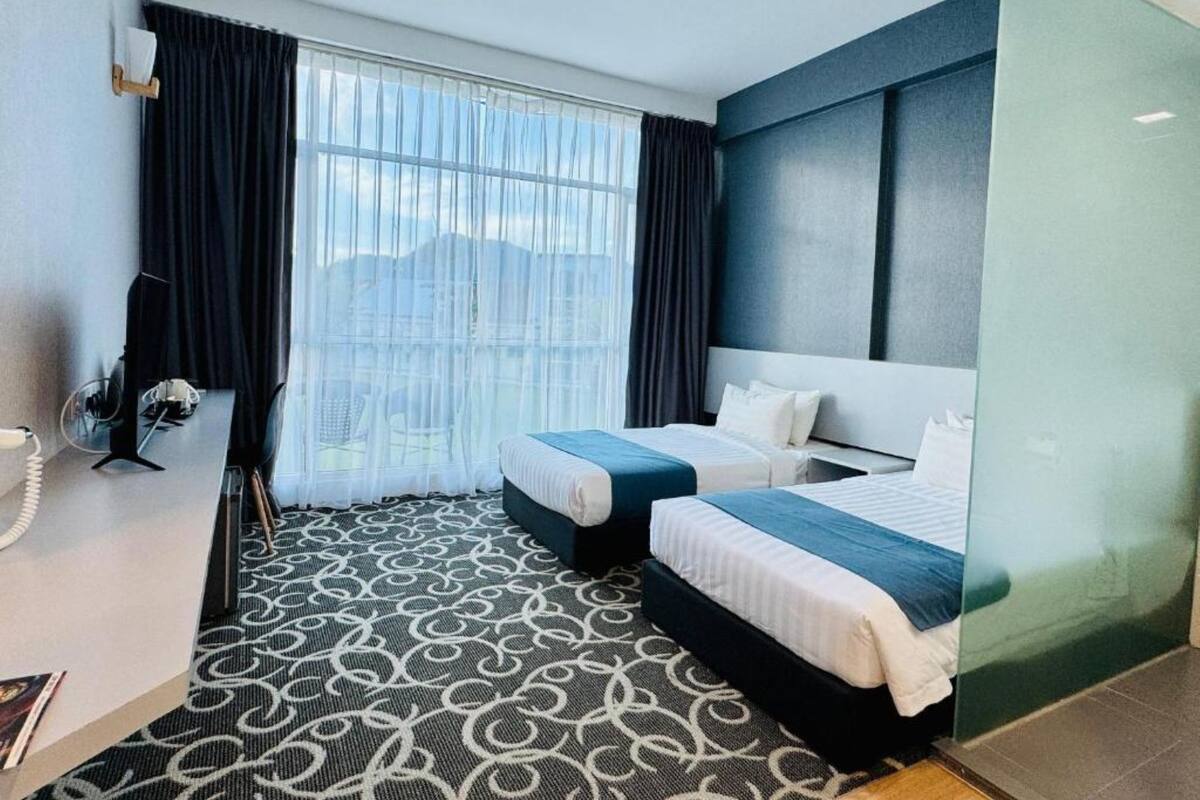 A hotel room with two beds, a desk, a chair, a telephone, and a large window with curtains.