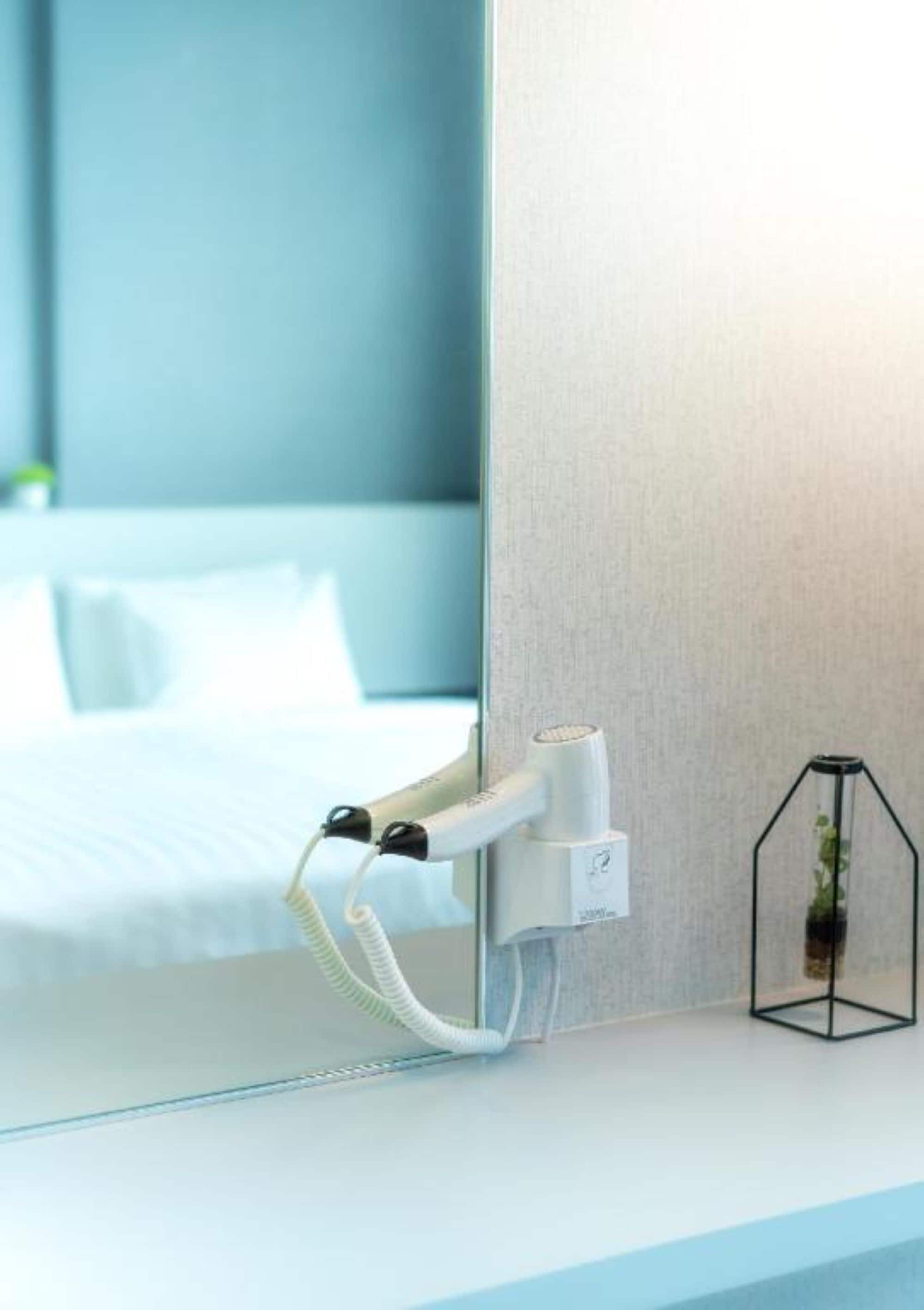 A modern hotel room with a large mirror, a hairdryer, and a small plant on the side table.