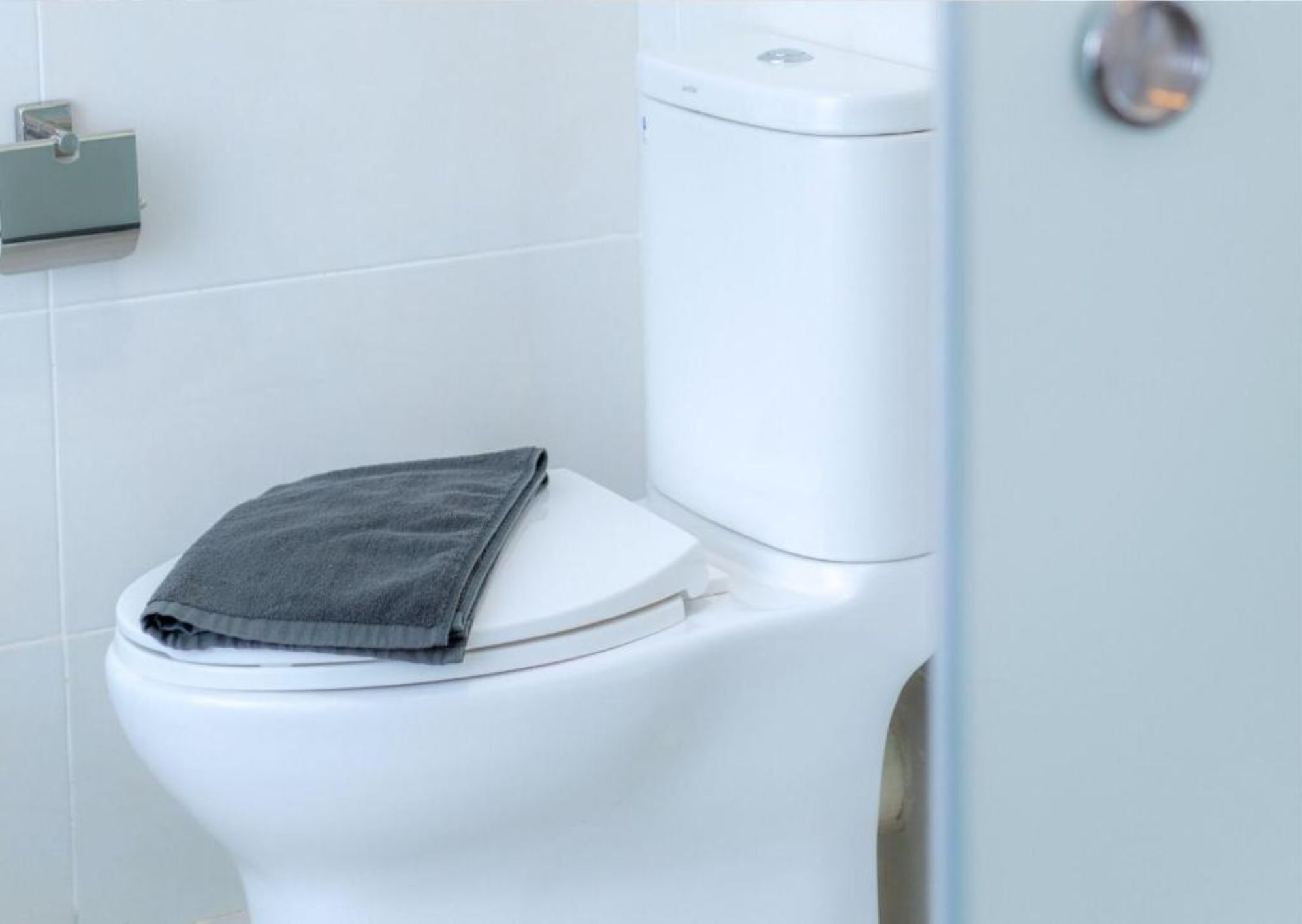 A white toilet with a grey towel on the lid.