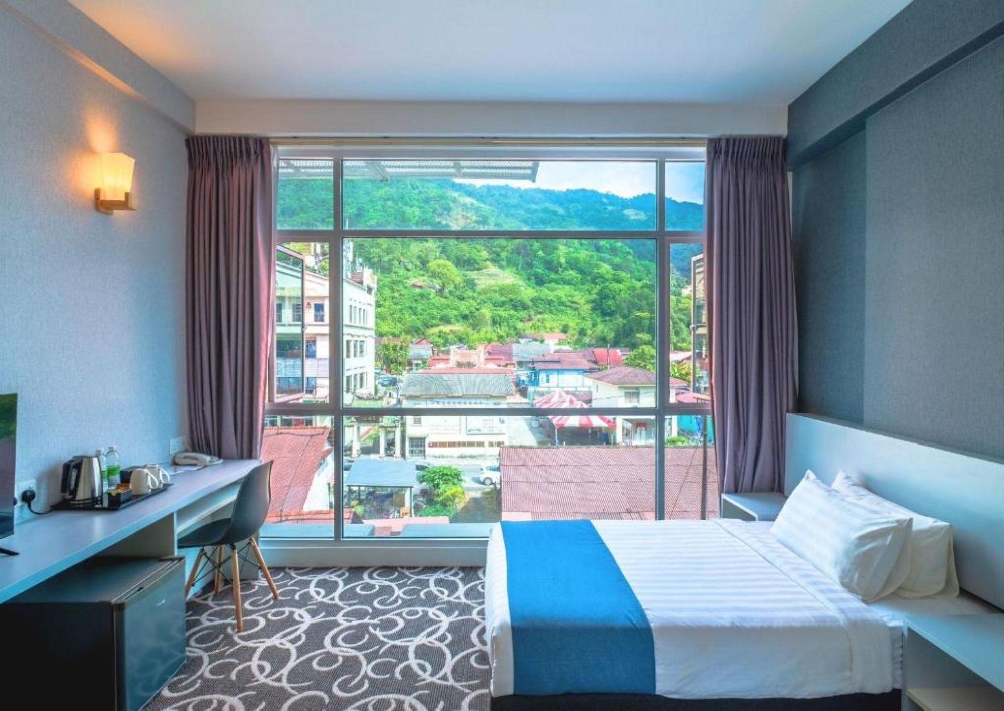 Ein Hotelzimmer mit großem Fenster, einem Bett, einem Schreibtisch und einem Stuhl.