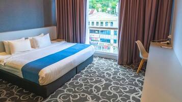 Habitación de hotel con cama, vistas a un paisaje urbano y alfombra estampada.