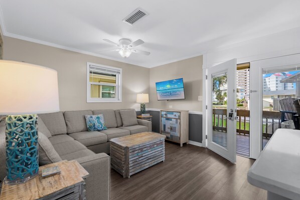 A living room with a sofa, coffee table, and a television. There is a door leading to an outdoor area.