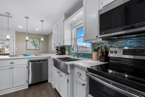 Una cocina moderna con electrodomésticos de acero inoxidable, muebles de cocina blancos y salpicadero con azulejos azules.