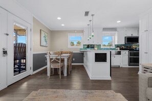 Una cocina moderna con armarios blancos, un comedor con sillas de madera y vistas al exterior a través de las ventanas.