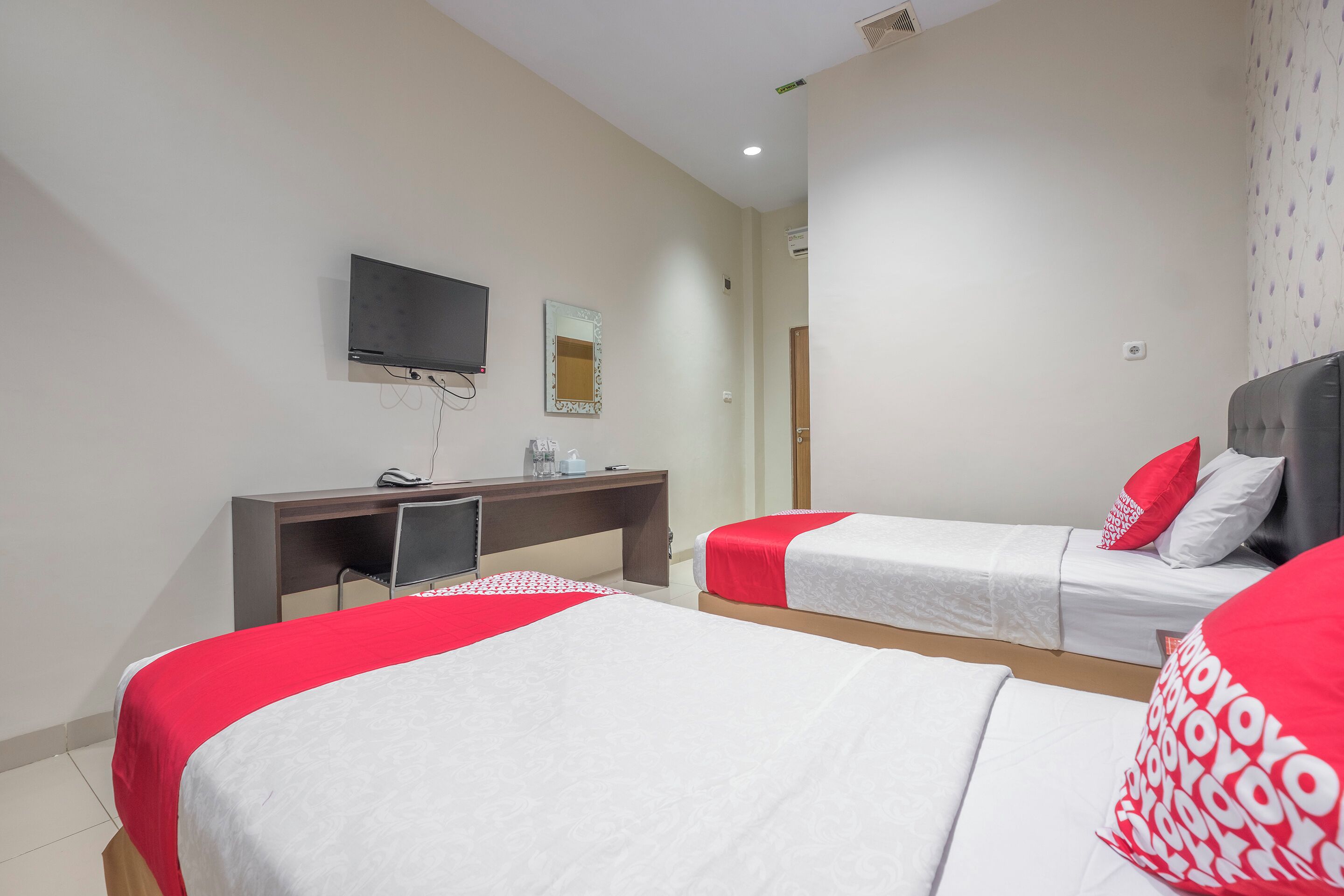 A hotel room with two beds, a desk with a TV, a mirror, and a door.