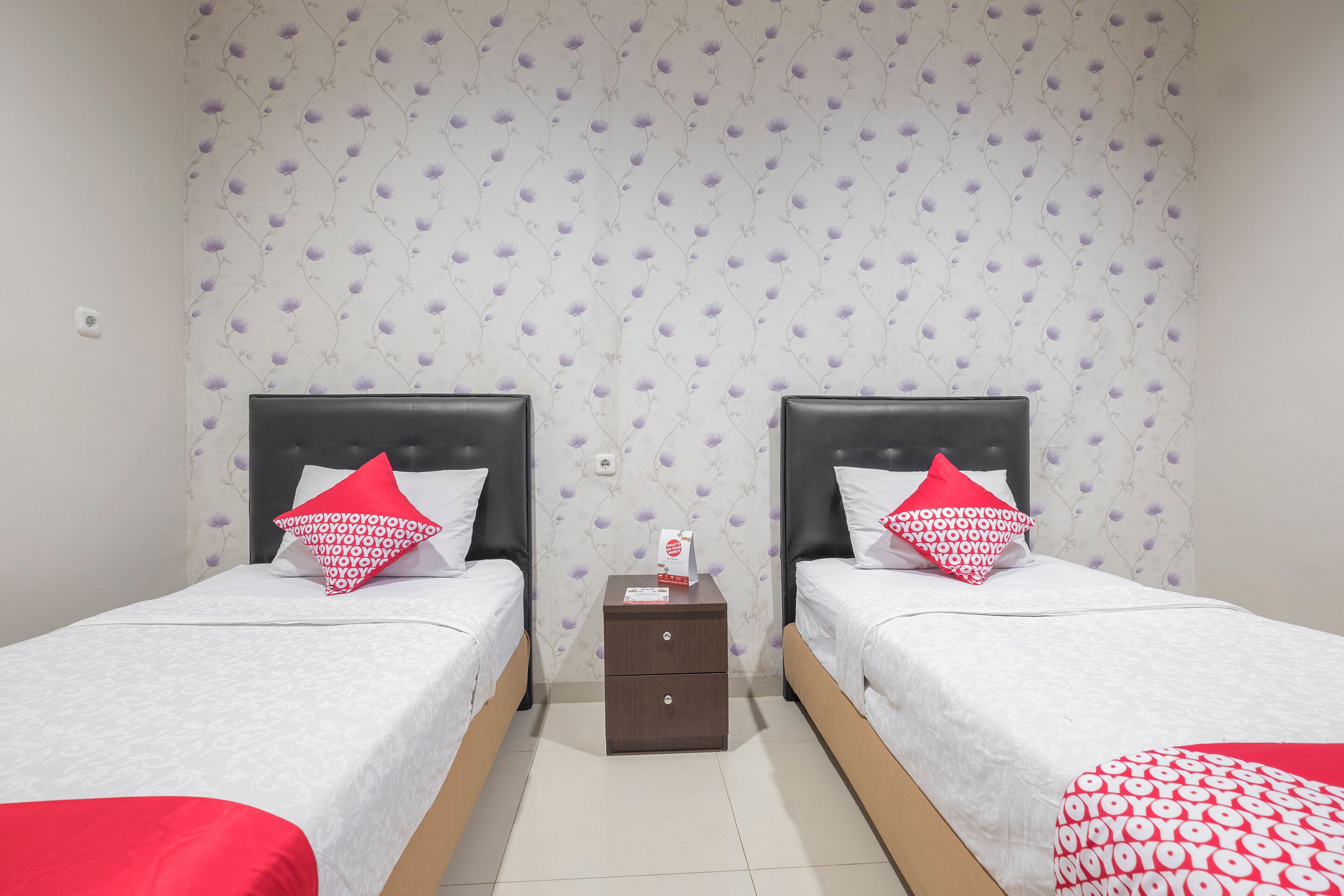 A room with two beds, each with a headboard, a small wooden nightstand, and a patterned wallpaper.