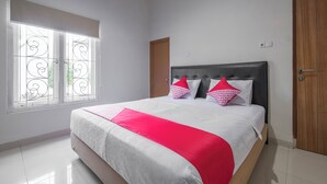 A bedroom with a bed, a window with decorative iron bars, a wooden door, and a white tiled floor. - Hotel O Makassar near Pantai Losari formerly Hotel Astra Novilia (Makassar)